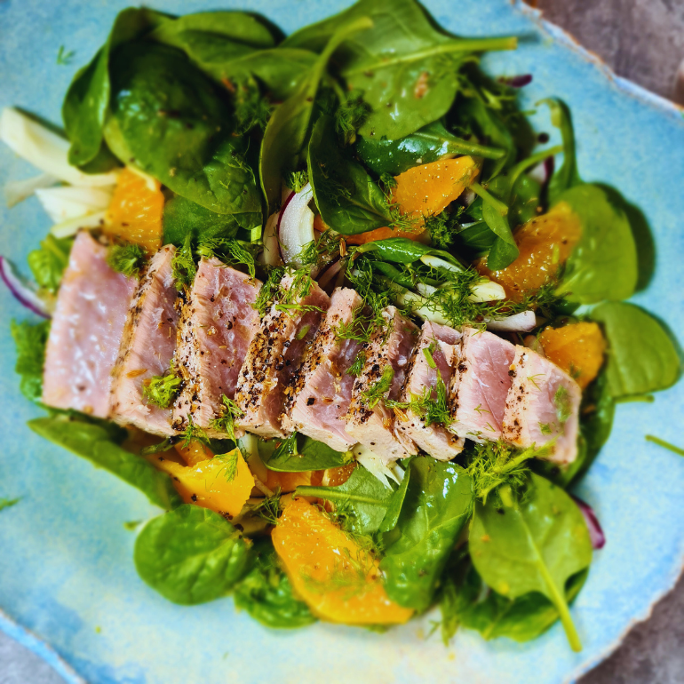 Seared sliced tuna on a bed of spinach, fennel and orange in a blue bowl