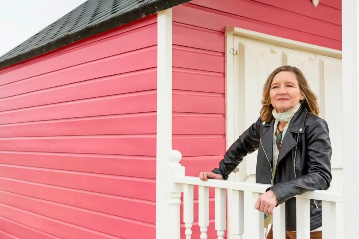 800x800 Nikkie Windsor, Integrated Nutritionist and Breath Coach, leaning on a railing outside a pink beach hut